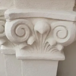 Dekoracyjny, świeżo otynkowany kapitel kolumny z ornamentami roślinnymi i spiralnymi wolutami, widoczny fragment rusztowania.