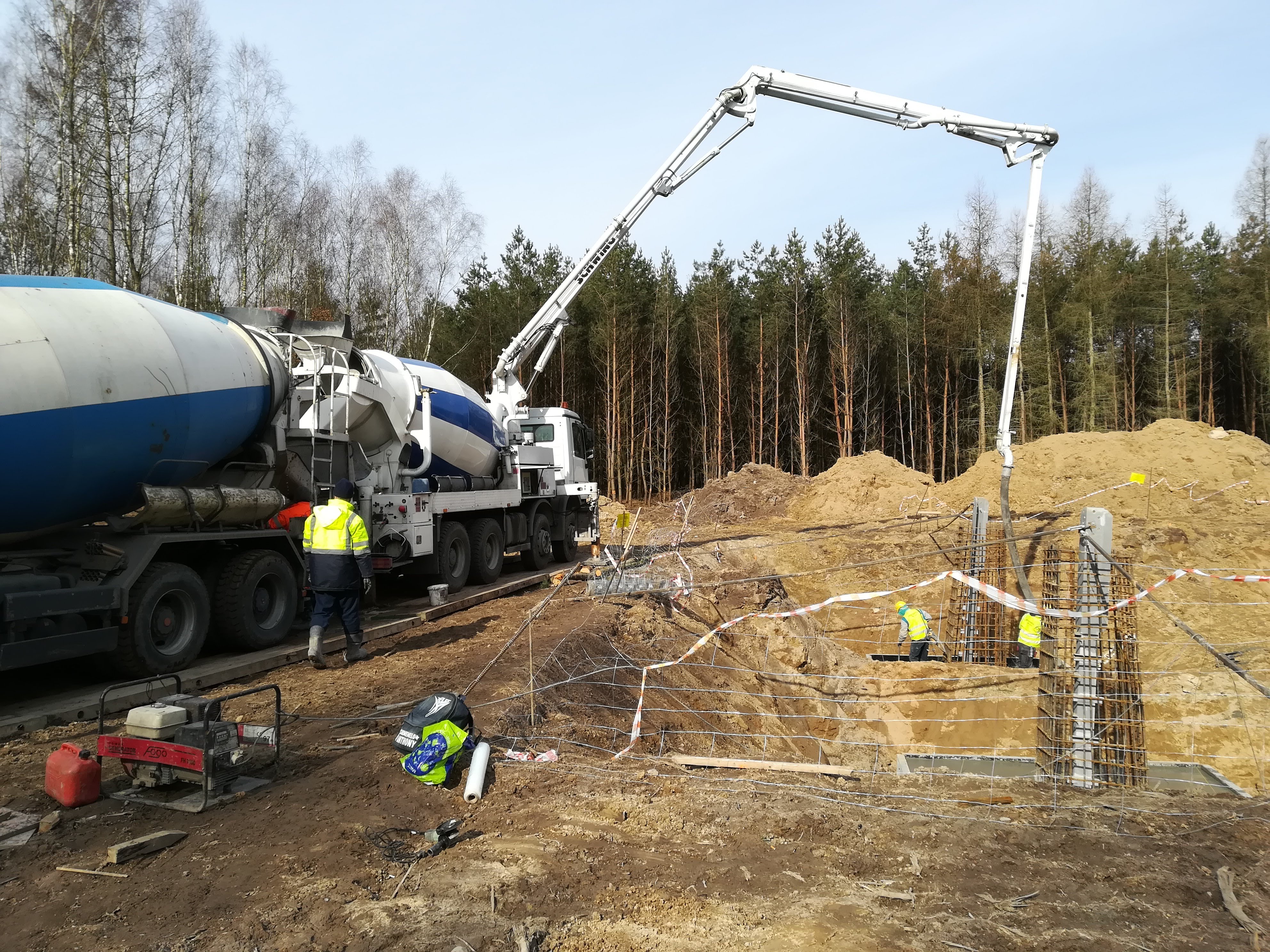 Betonowa pompa podaje mieszankę do szalunków zbrojeniowych na placu budowy, w tle las i niebo.