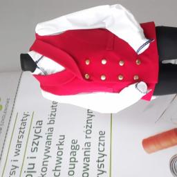 Centrum Szkoleniowe Prestigo - Czerwona kamizelka z złotymi guzikami i białą koszulą na manekinie, obok leżą akcesoria krawieckie: nici, miarka krawiecka. W tle widoczne logo centrum szkoleniowego.