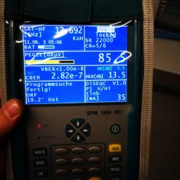 Volt Electro - Miernik sygnału satelitarnego SPM 1600 HD z wyświetlaczem pokazującym parametry sygnału, w tle widoczne kable i elementy instalacji.