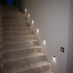 Volt Electro - Surowe betonowe schody z zamontowanymi, kwadratowymi lampkami LED w ścianie, widoczne przewody elektryczne, instalacja w trakcie realizacji.