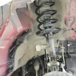 Szczegółowe ujęcie zawieszenia samochodu w trakcie naprawy w Olzie, widoczna sprężyna i amortyzator, elementy nadkola z widocznymi śladami użytkowania i korozji.