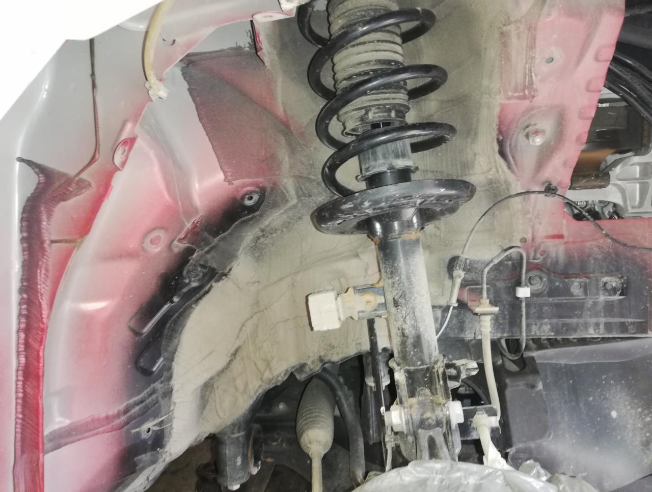 Szczegółowe ujęcie zawieszenia samochodu w trakcie naprawy w Olzie, widoczna sprężyna i amortyzator, elementy nadkola z widocznymi śladami użytkowania i korozji.