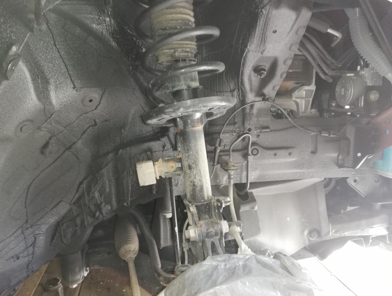 Podwozie samochodu po zabezpieczeniu antykorozyjnym, widoczny element zawieszenia i czarna, gruba powłoka ochronna na nadkolu.