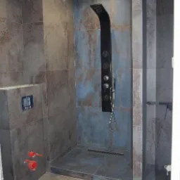 Nowoczesna kabina prysznicowa z czarnym panelem natryskowym i odpływem liniowym, wykończona płytkami w odcieniach szarości i błękitu z efektem rdzy.