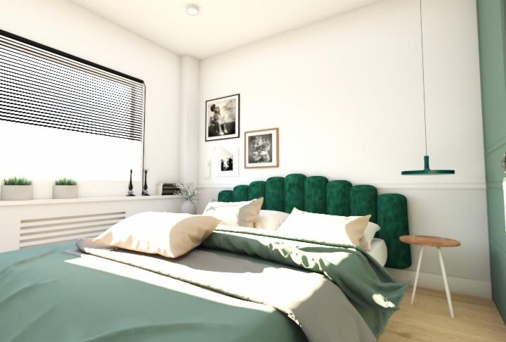 Jasna sypialnia z zielonym, aksamitnym zagłówkiem, minimalistyczną lampą wiszącą i dekoracjami ściennymi, oświetlona naturalnym światłem z okna z żaluzjami.