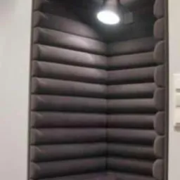 Wnęka ścienna wyłożona ciemnoszarą tapicerką z poziomymi przeszyciami, oświetlona lampą, z poduszką wałkiem i okrągłą poduszką na siedzisku.