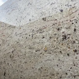 Fragment płyty z jasnego kamienia z drobnymi, ciemnymi plamkami i delikatnymi, poziomymi smugami.