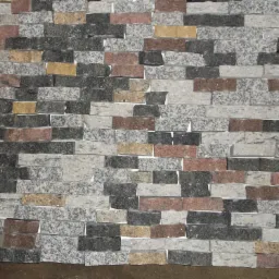 Ściana wykończona mozaiką z drobnych, prostokątnych płytek kamiennych w odcieniach szarości, bieli, brązu i beżu, ułożonych warstwowo.