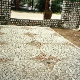 Ułożona kostka granitowa w okrągłe wzory przed bramą wjazdową, widoczne niedoskonałości i zabrudzenia na powierzchni.