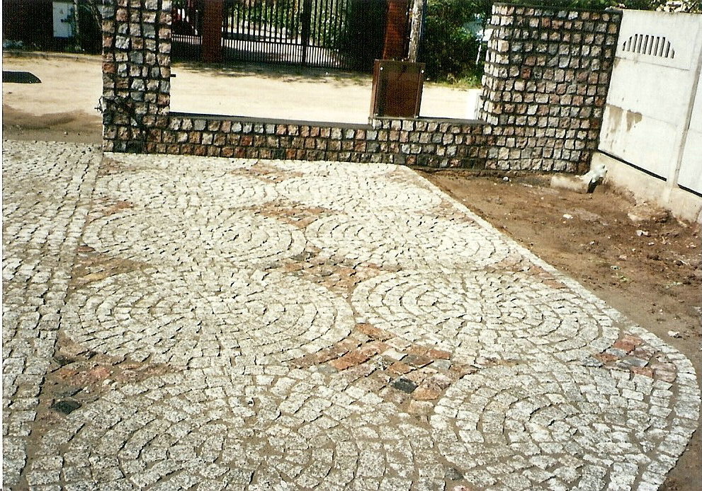 Ułożona kostka granitowa w okrągłe wzory przed bramą wjazdową, widoczne niedoskonałości i zabrudzenia na powierzchni.