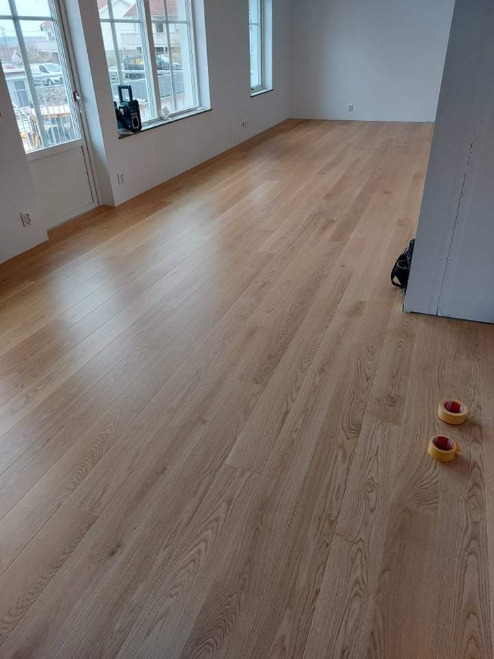 Jasne panele podłogowe ułożone w nowym pomieszczeniu z dwoma rolkami taśmy malarskiej w prawym dolnym rogu i narzędziem na parapecie okna.