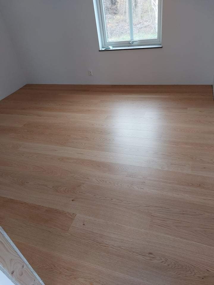 Jasne panele podłogowe w pokoju na poddaszu z oknem dachowym, widoczne delikatne usłojenie drewna i odbicie światła.