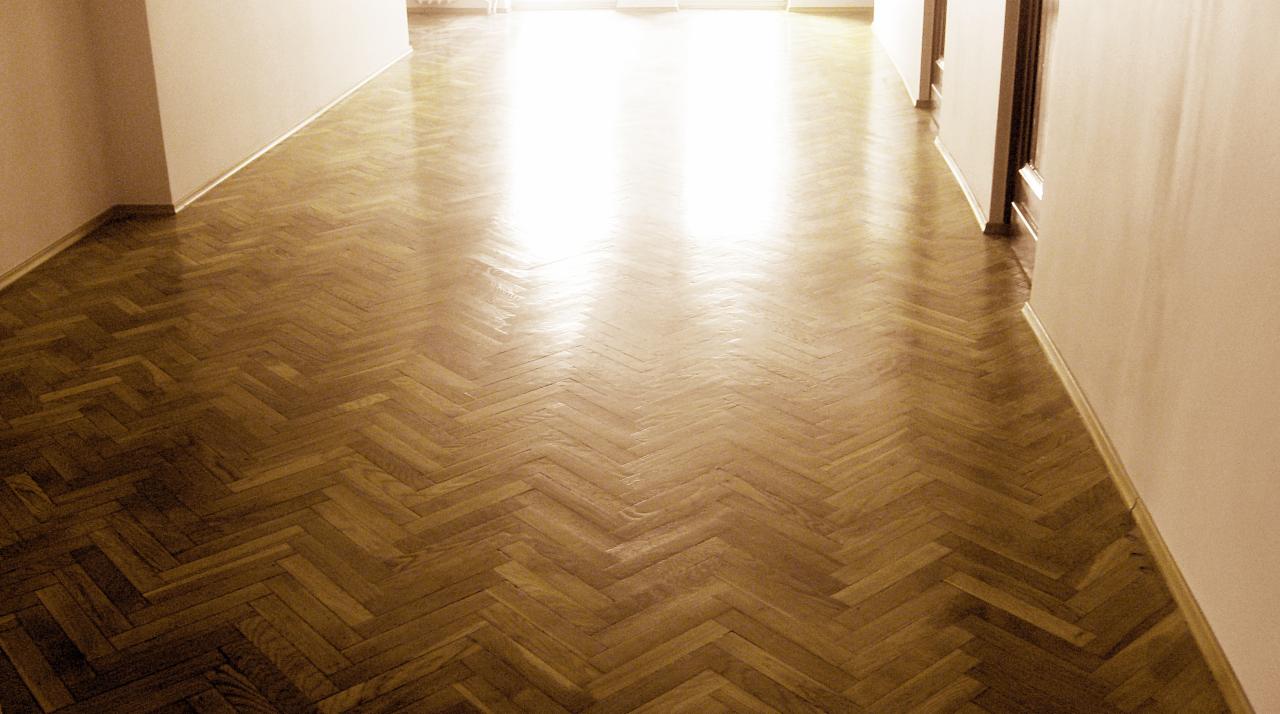 Wycyklinowany parkiet ułożony w jodełkę, widok z perspektywy wejścia do pomieszczenia, z wyraźnym połyskiem i refleksami świetlnymi.