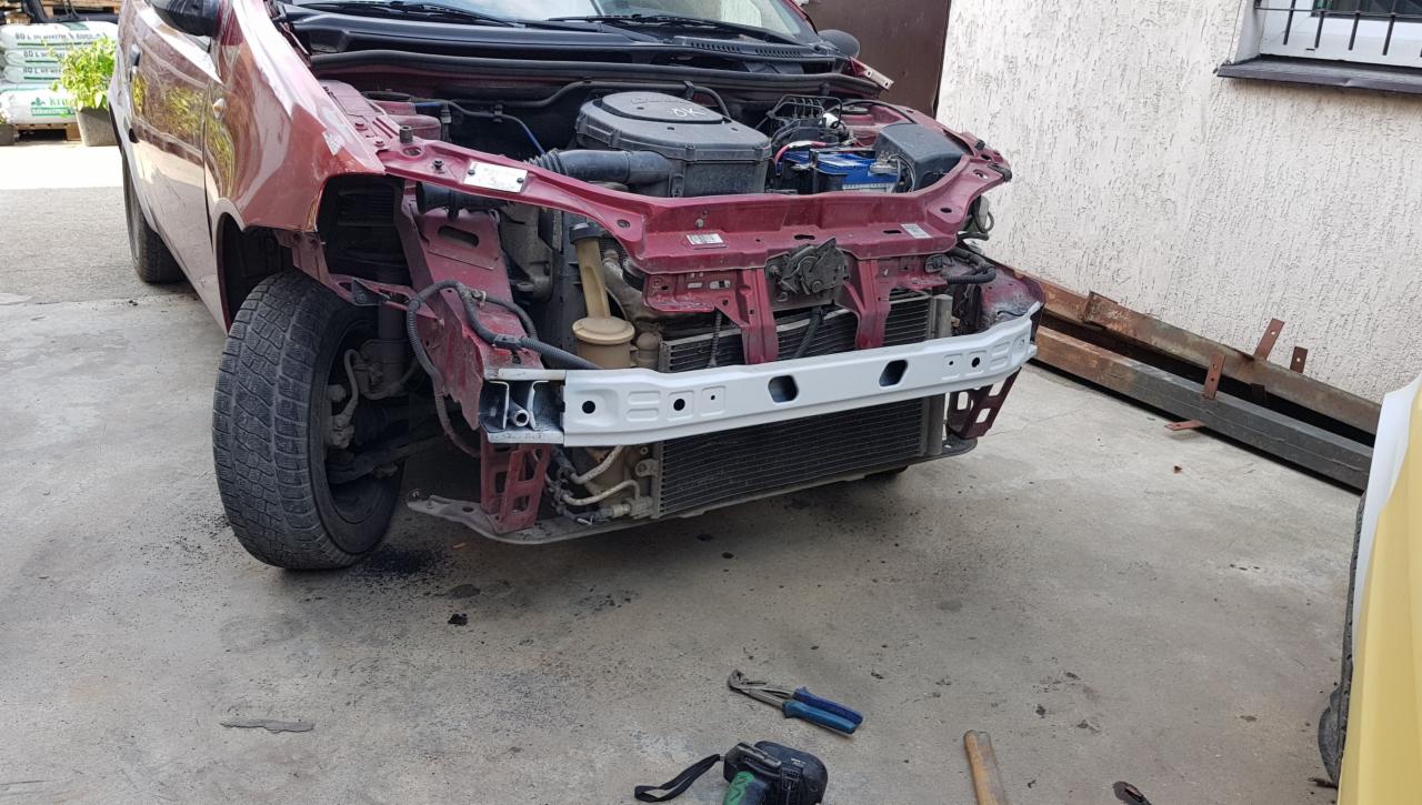 Czerwony samochód w trakcie naprawy karoserii, z widocznym silnikiem i częściowo zdemontowanym przodem, na betonowym podłożu leżą narzędzia.