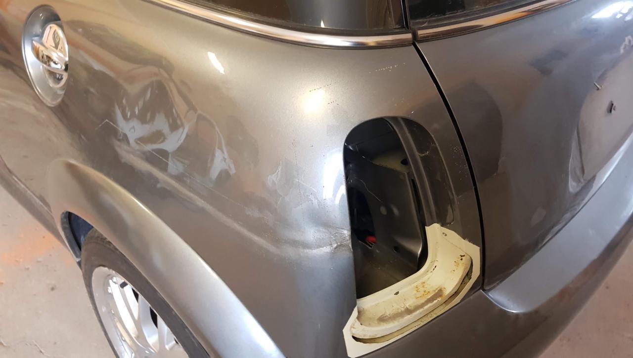 Uszkodzony błotnik samochodu Mini Cooper z widocznymi wgnieceniami, rysami i śladami szpachli, przygotowany do lakierowania. Klapka wlewu paliwa zdemontowana.