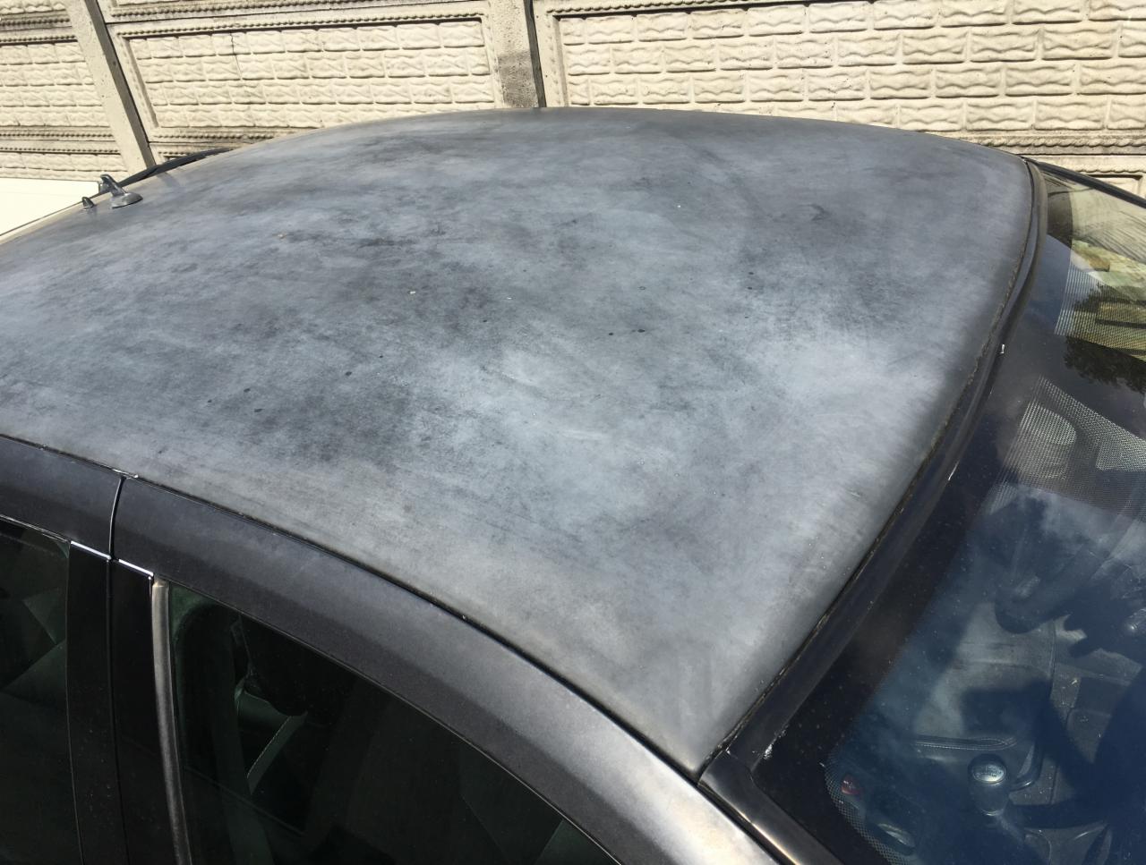 Zmatowiały dach samochodu z widocznymi śladami korozji i odbarwieniami, na tle betonowego muru.