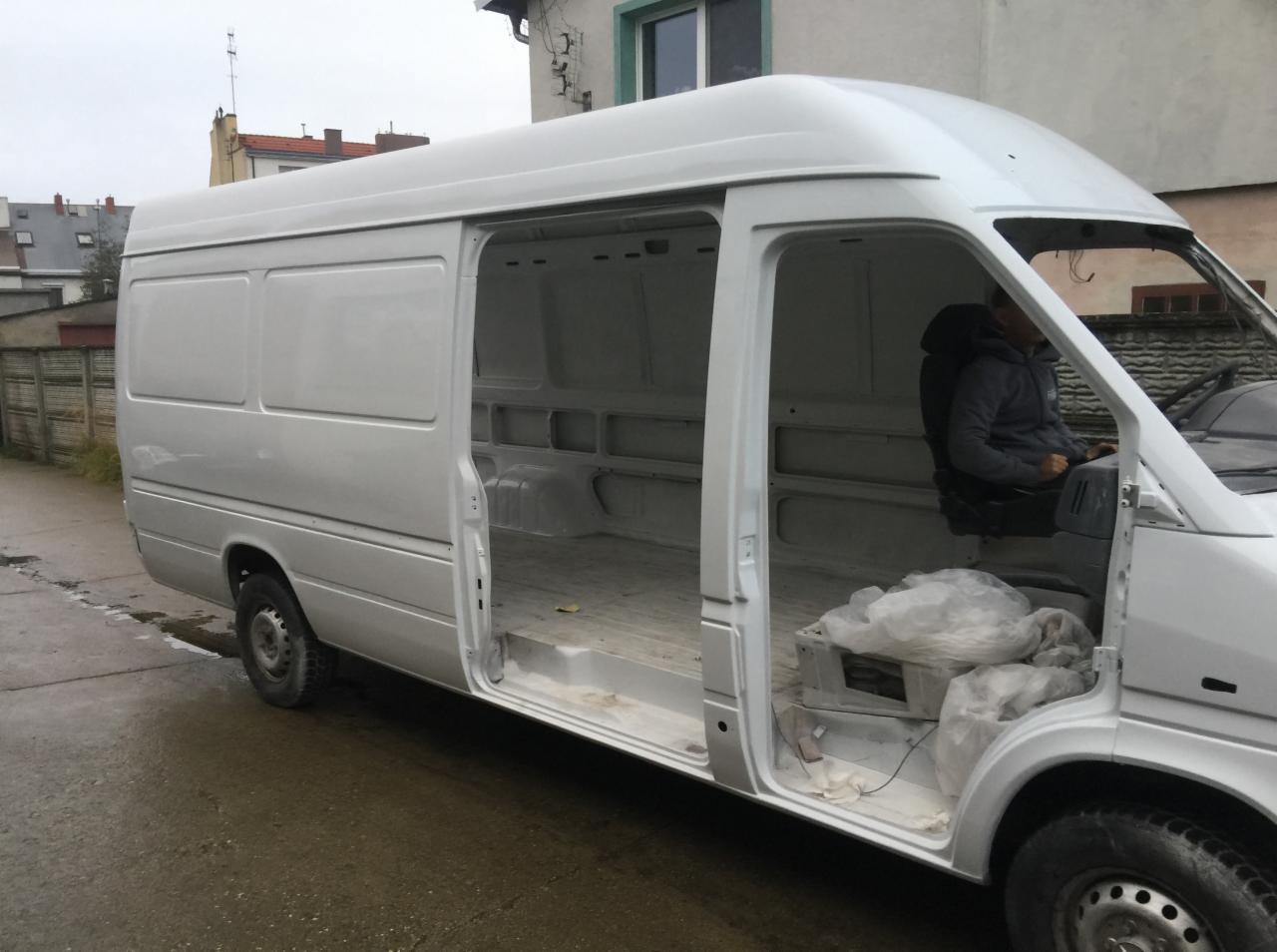 Biały samochód dostawczy po świeżym lakierowaniu, z otwartymi drzwiami bocznymi i widocznym wnętrzem, na zewnątrz budynku.