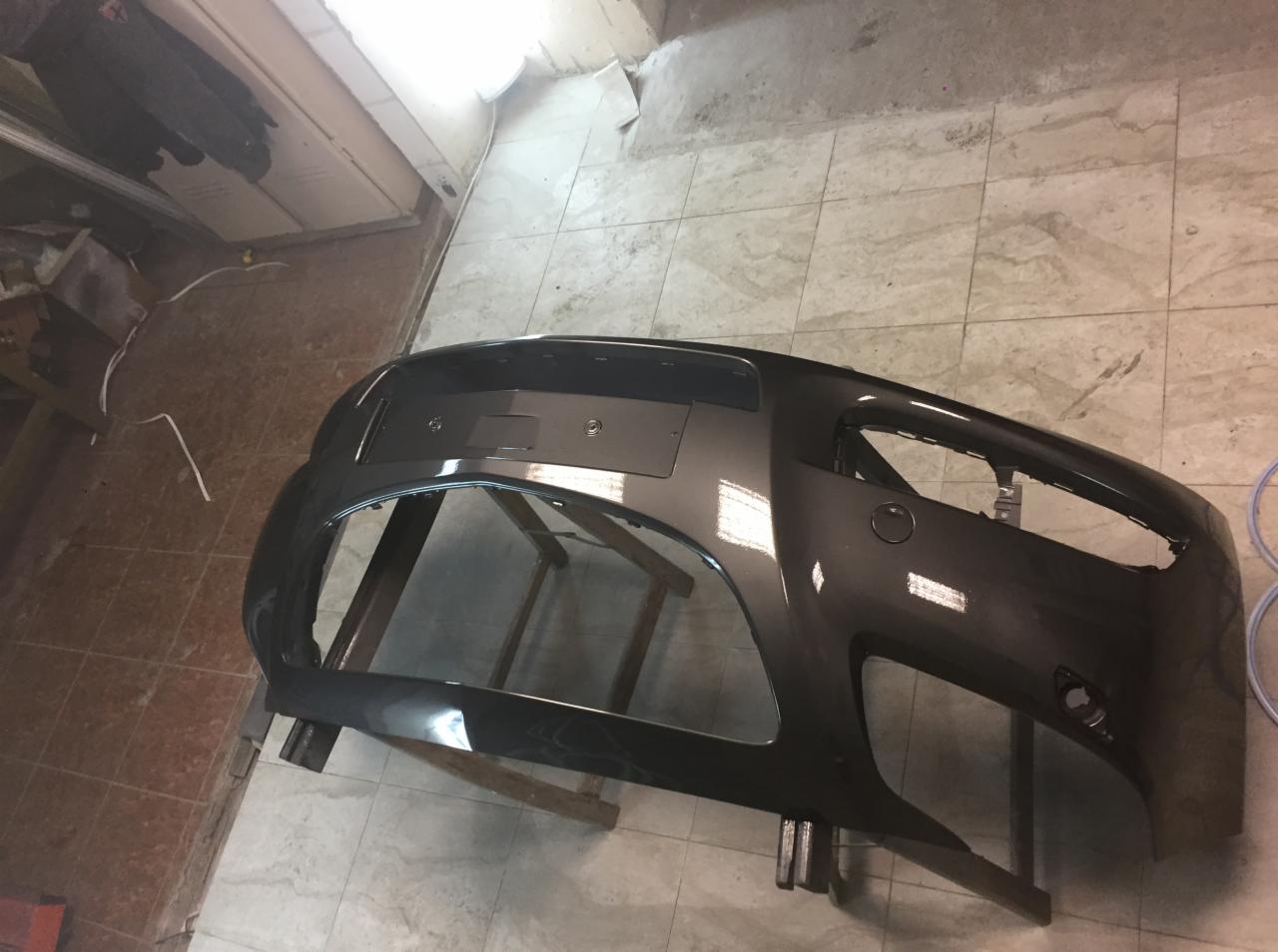 Szary, odnowiony zderzak samochodowy na stojaku w warsztacie, widoczne ślady obróbki.