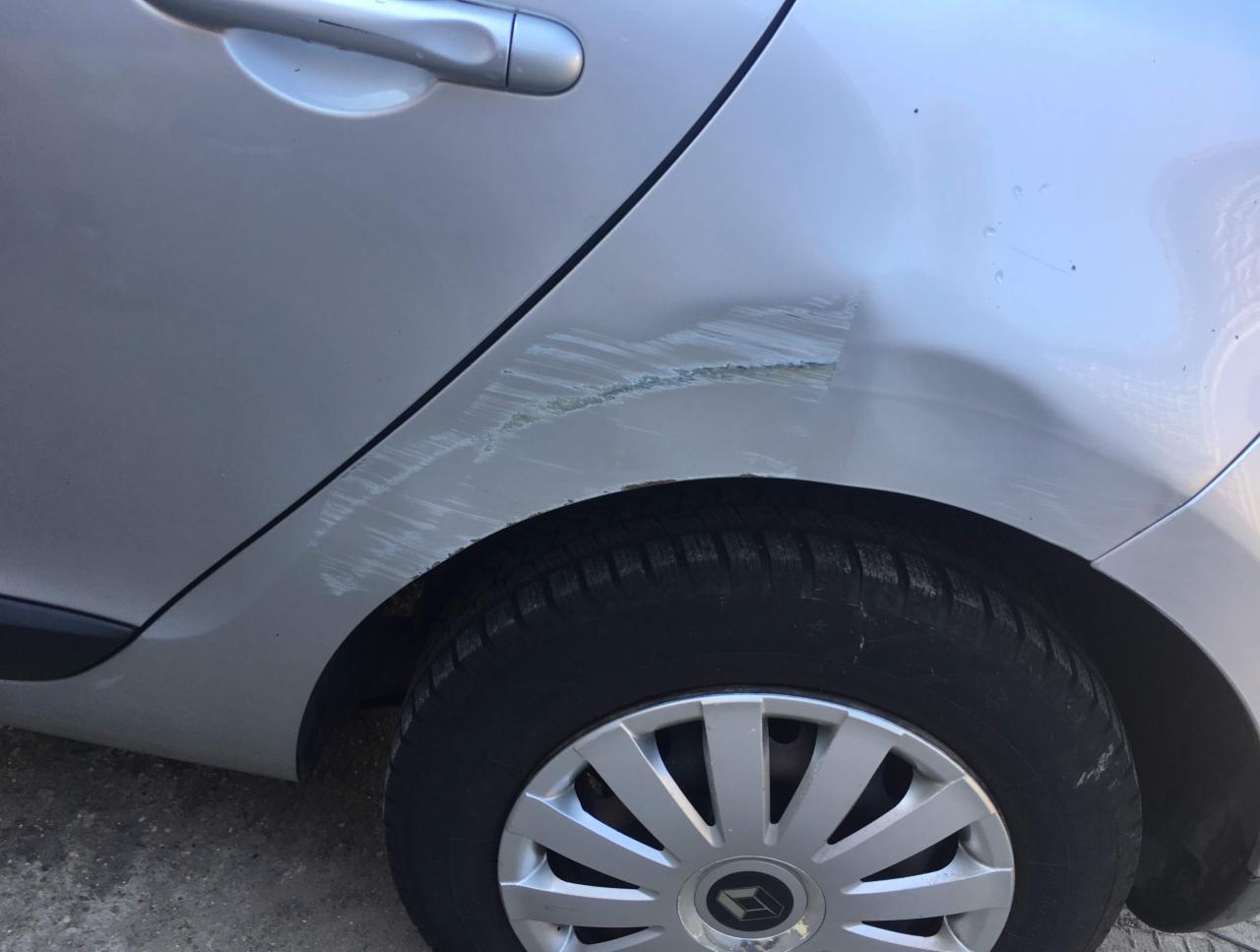 Srebrny samochód z uszkodzeniami lakieru i wgnieceniem na tylnym błotniku, widoczne ślady po szlifowaniu.