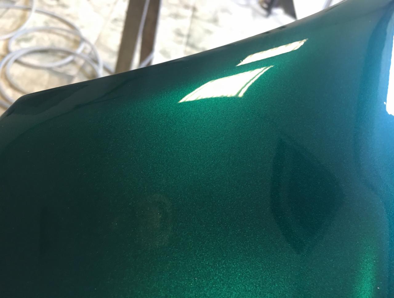 Szmaragdowy, metaliczny lakier samochodowy z wyraźnym odbiciem światła, widoczne drobne ziarno lakieru.