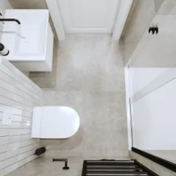 Widok z góry na minimalistyczną łazienkę z białymi płytkami, umywalką z czarną armaturą, toaletą, prysznicem ze szklaną ścianką oraz dekoracyjnymi elementami jak mydła i dyfuzor zapachowy.