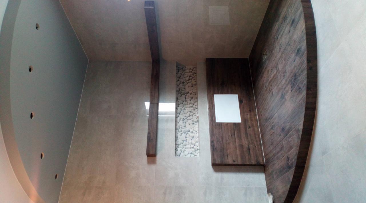 Nowoczesna łazienka z drewnianymi elementami, wnęką wypełnioną białymi kamieniami i okrągłym sufitem z punktowym oświetleniem.