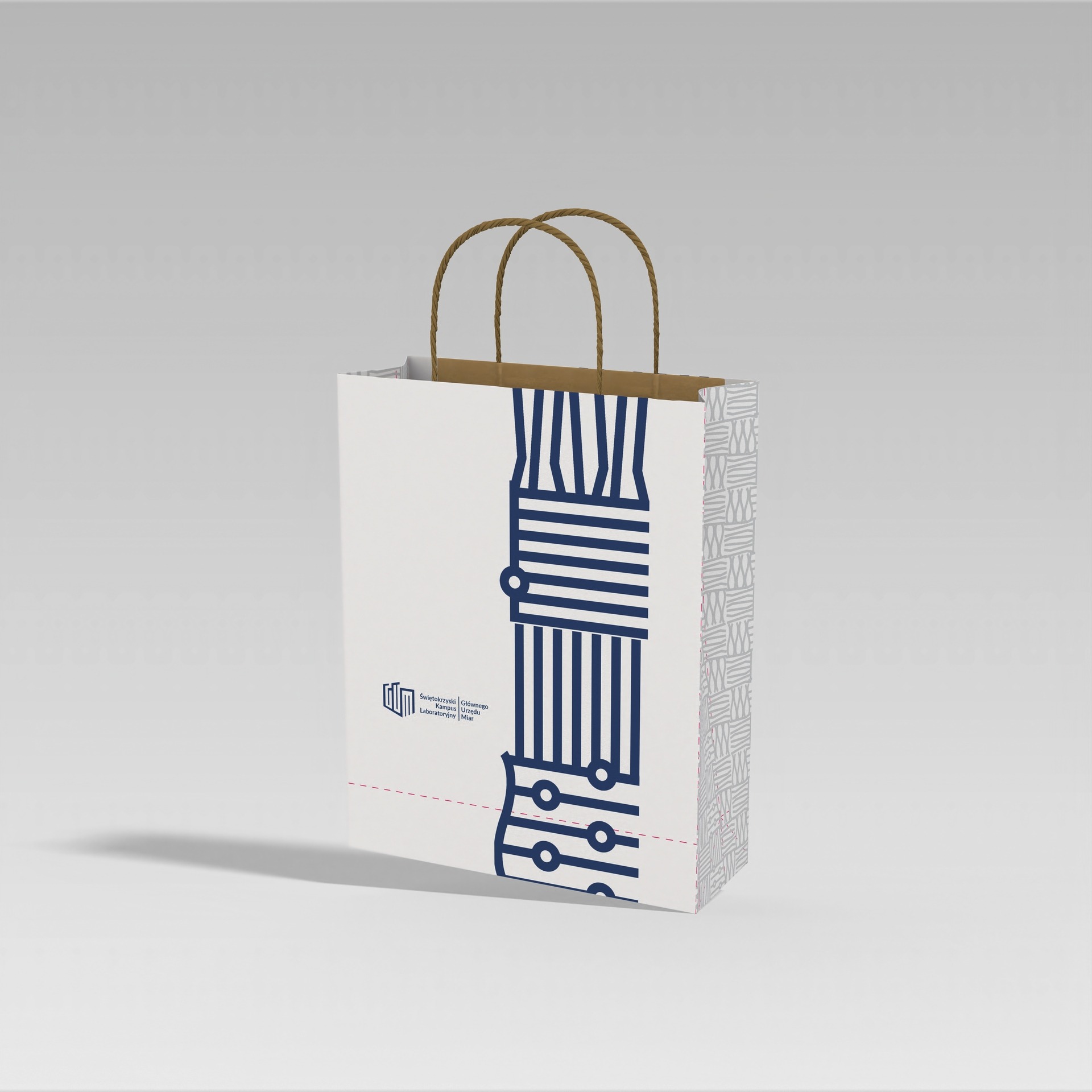 Biała papierowa torba z niebieskim abstrakcyjnym wzorem przypominającym schemat elektryczny oraz logo Świętokrzyskiego Kampusu Laboratoryjnego na jasnoszarym tle.