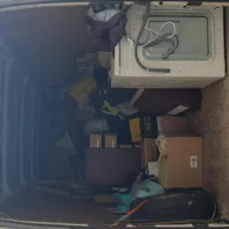 Wnętrze przestrzeni ładunkowej białego busa wypełnione kartonami, pralką, oponą i różnymi przedmiotami podczas przeprowadzki.