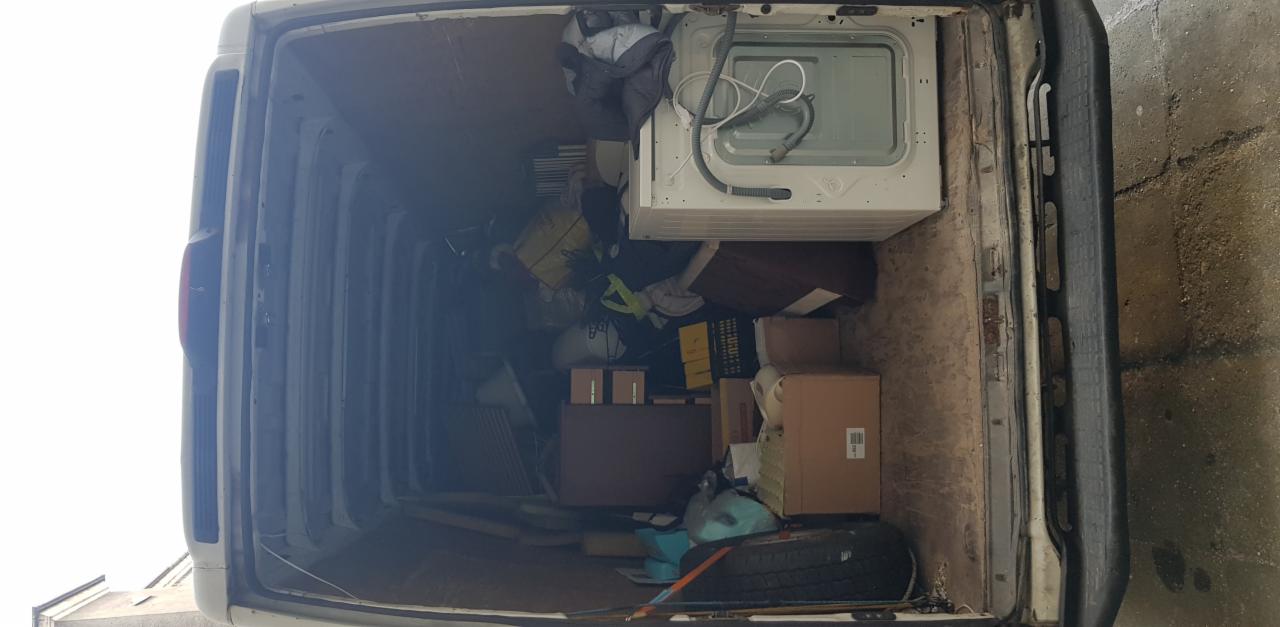 Wnętrze przestrzeni ładunkowej białego busa wypełnione kartonami, pralką, oponą i różnymi przedmiotami podczas przeprowadzki.