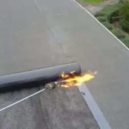 Prace dekarskie: zgrzewanie papy termozgrzewalnej na płaskim dachu za pomocą palnika gazowego. Widoczne łączenia papy.