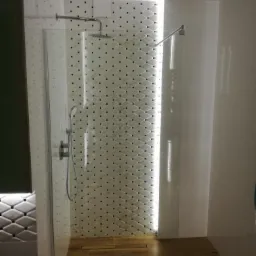 Nowoczesna kabina prysznicowa z odpływem liniowym w podłodze, wykończona białymi płytkami z czarnymi akcentami, podświetlona listwą LED.