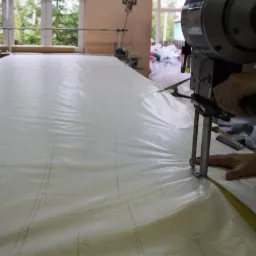 Elektryczny nóż krojczy w trakcie cięcia kilku warstw materiału z naniesionymi szablonami, widoczna ręka operatora.