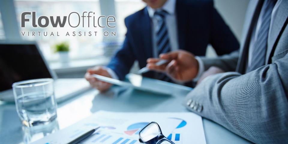 Dwóch mężczyzn w garniturach omawia wykresy na tablecie, na biurku leżą okulary, szklanka wody i laptop, w tle logo firmy FlowOffice.