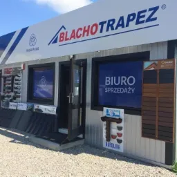 Fasada biura sprzedaży blachy trapezowej w Zamościu z otwartymi drzwiami, eksponowane próbki produktów na zewnątrz budynku.