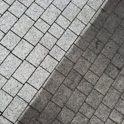 ALIGATOR Alicja Gatlik - Ukończona nawierzchnia z kostki brukowej, widoczny kontrast czystej i zabrudzonej powierzchni, ułożona pod kątem, szara kolorystyka.