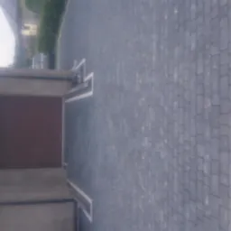 Ułożona szara kostka brukowa tworząca podjazd do garażu, z widocznymi białymi obrzeżami i fragmentem posesji w tle.