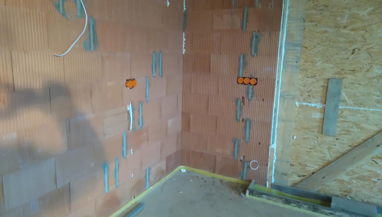 Wewnętrzne ściany z cegły z wywierconymi otworami na puszki elektryczne i poprowadzonymi przewodami, zabezpieczone zaprawą.