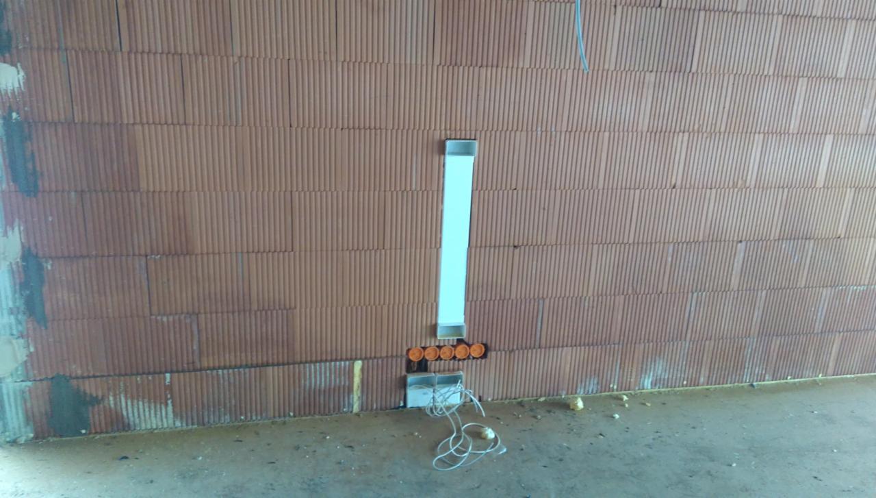 Wnęka w surowej ścianie z cegły wypełniona pionowym kanałem instalacyjnym i puszkami elektrycznymi z przewodami.