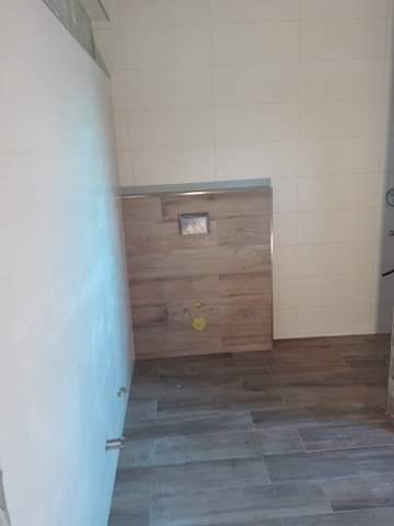 Układanie płytek imitujących drewno na podłodze i ścianie w łazience w Człuchowie, widoczne przygotowane otwory na instalacje.