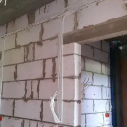 Białe przewody elektryczne ułożone w peszlach na surowych ścianach z betonu komórkowego w trakcie budowy domu, widoczne puszki elektryczne.