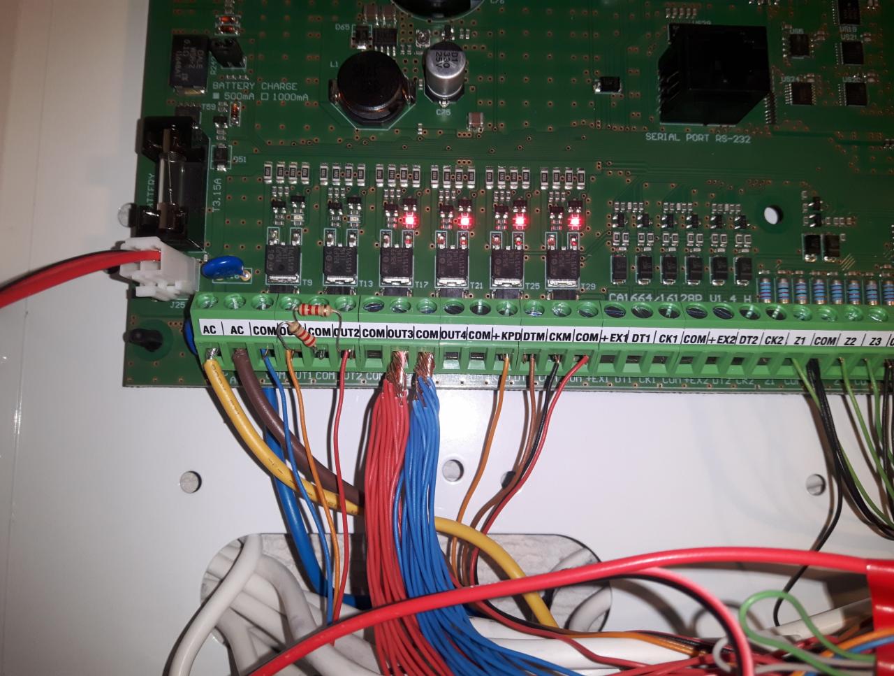 Podłączenie przewodów do płyty głównej systemu alarmowego z widocznymi diodami LED i oznaczeniami złącz, w trakcie instalacji w obudowie.