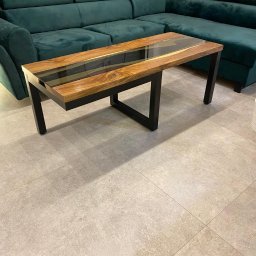 HolMat - Stolik kawowy z blatem z drewna i żywicy epoksydowej, czarne metalowe nogi, na tle zielonego narożnika.