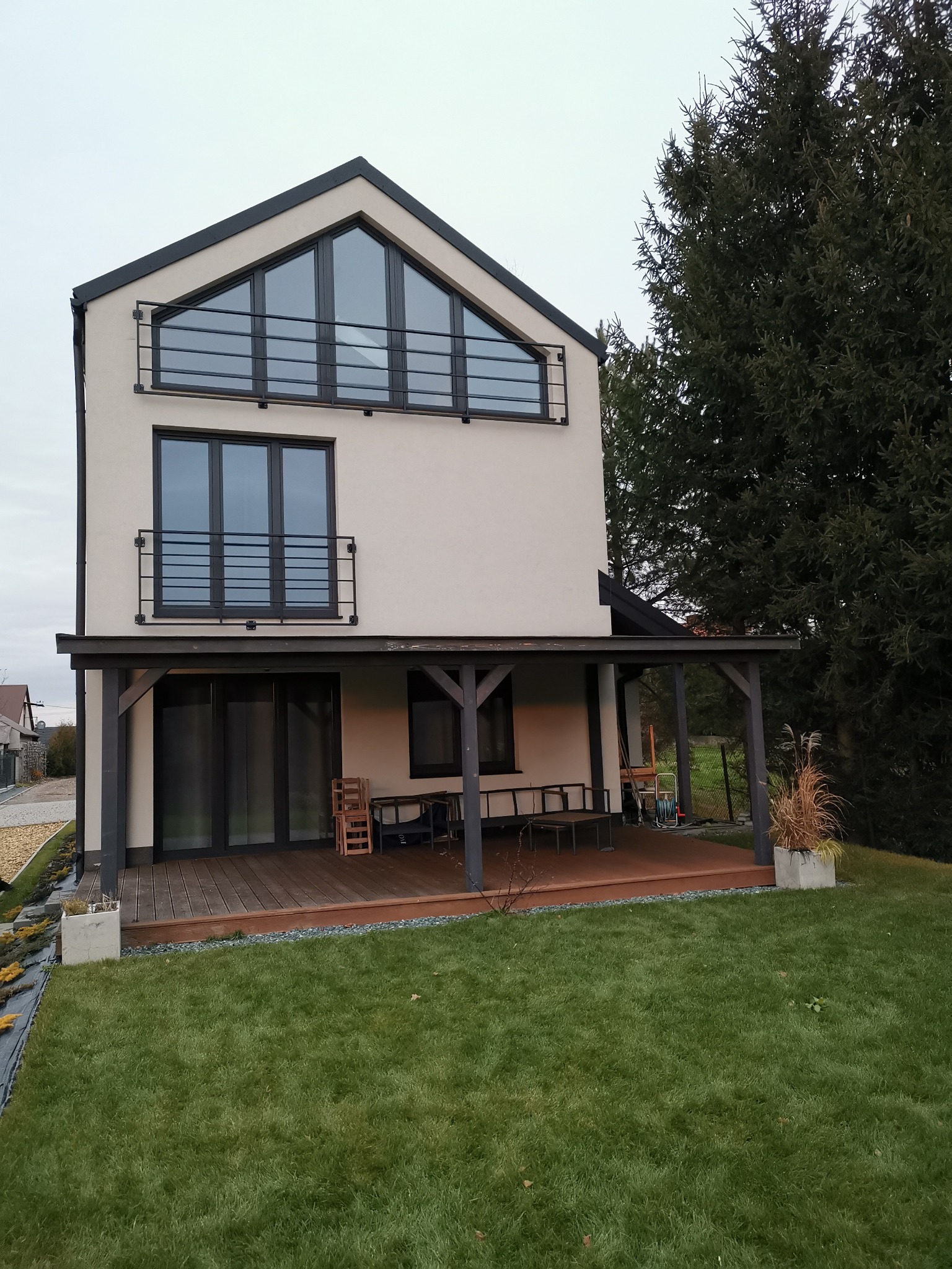 Dwupiętrowy dom z kremową elewacją i czarnymi, metalowymi poręczami balkonowymi na każdym piętrze, widok z ogrodu z zadbanym trawnikiem.
