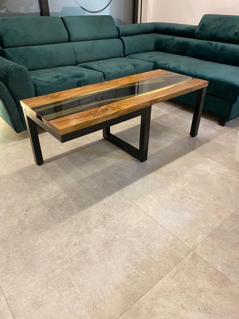 Stolik kawowy z blatem z drewna i żywicy epoksydowej, czarne metalowe nogi, na tle zielonego narożnika.