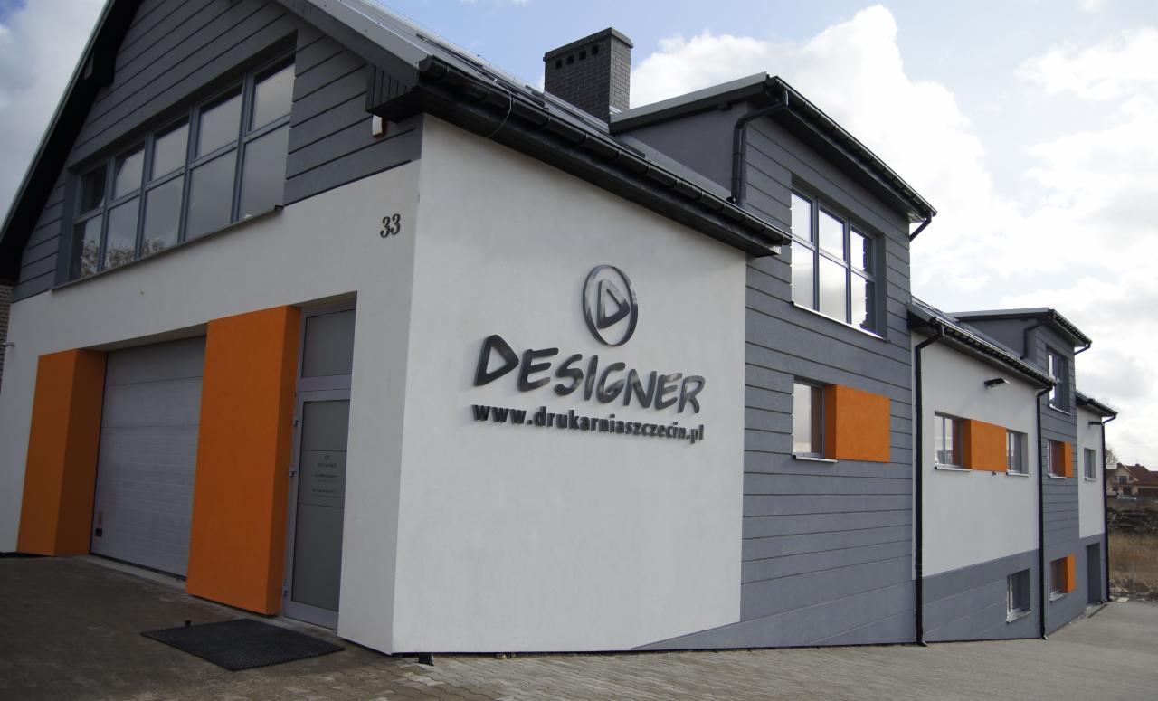 Budynek drukarni z szarymi i białymi elewacjami, z czarnym napisem 'DESIGNER www.drukarniaszczecin.pl' i pomarańczowymi akcentami przy oknach i bramie garażowej.