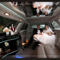 Para młoda w limuzynie: panna młoda w białej sukni z bukietem, pan młody w czarnym garniturze, wnętrze z barkiem i lustrzanym sufitem.