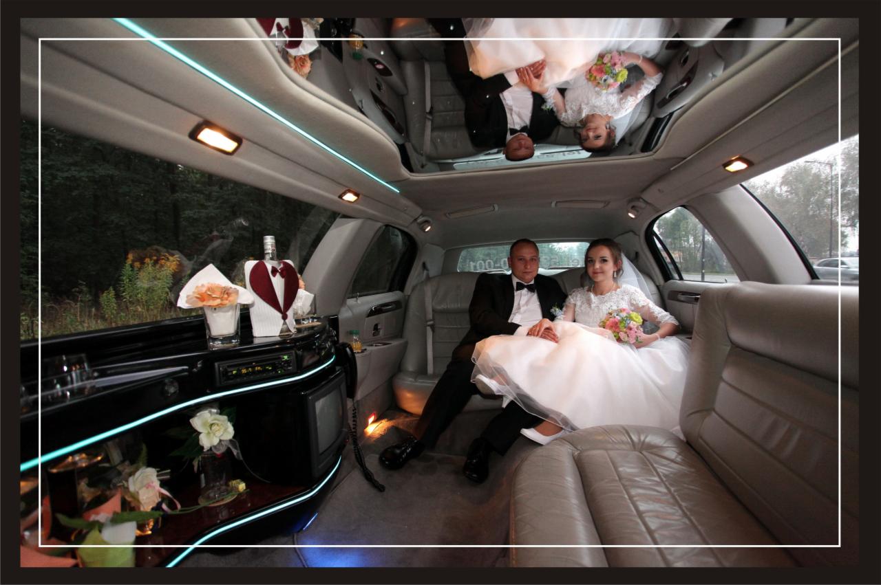 Para młoda w limuzynie: panna młoda w białej sukni z bukietem, pan młody w czarnym garniturze, wnętrze z barkiem i lustrzanym sufitem.