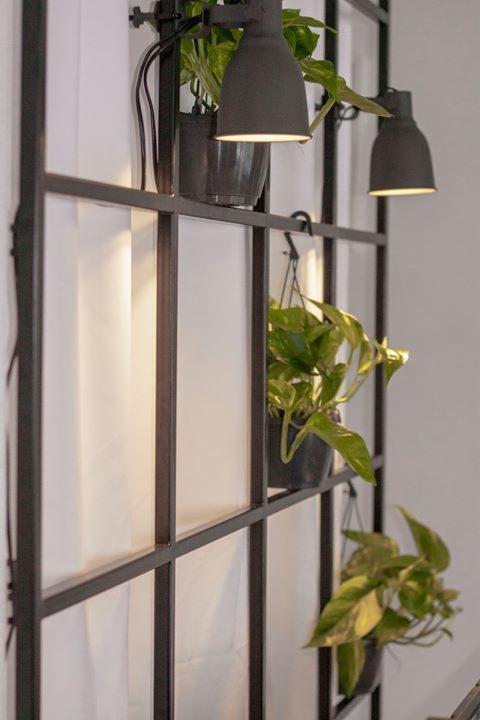 Metalowa konstrukcja w stylu industrialnym z zamontowanymi lampami i roślinami doniczkowymi, białe tło.