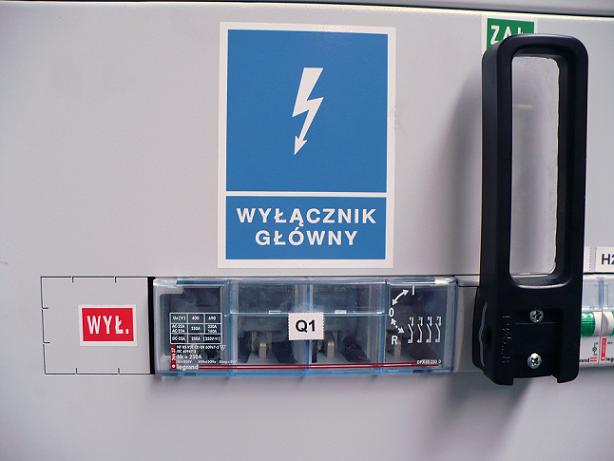 Tablica elektryczna z wyłącznikiem głównym, oznaczeniem WYŁ. i symbolem błyskawicy na niebieskim tle.